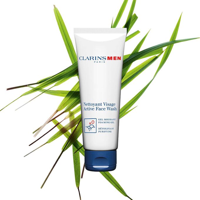 Packshot of the Active Face Wash, men's face cleanser by Clarins next to bison grass to emphasize its key ingredient.