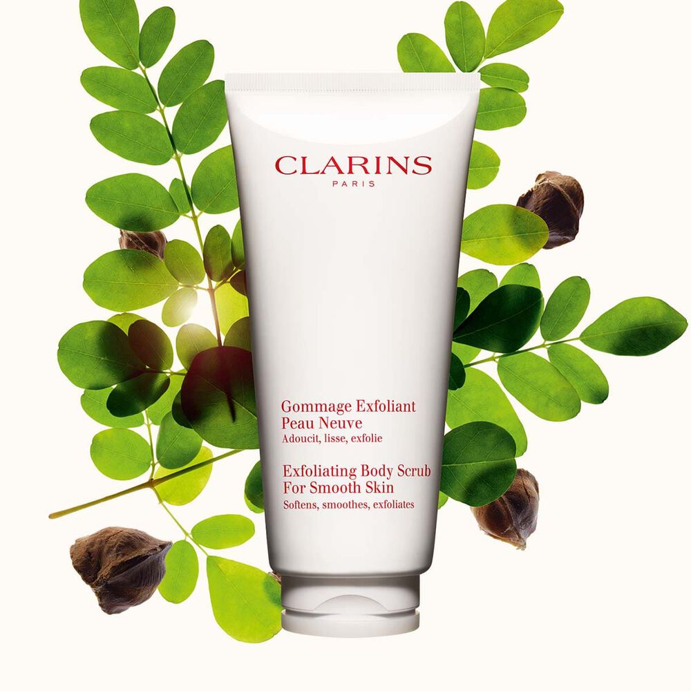 Packshot of Clarins Exfoliating Body Scrub for Smooth Skin placed next to moringa nuts on a light beige background