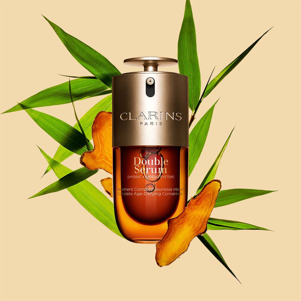 Packshot of the Clarins Double Serum displayed in front of its ingredient, including curcuma, on a gold background