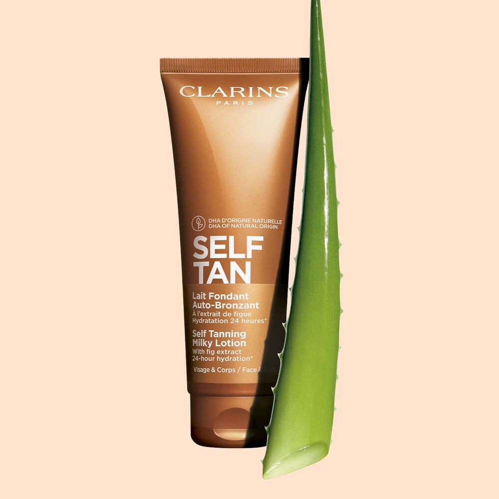 Packshot of a tube of Clarins Self Tanning Milky Lotion close to a piece of aloe vera on a pale orange background.