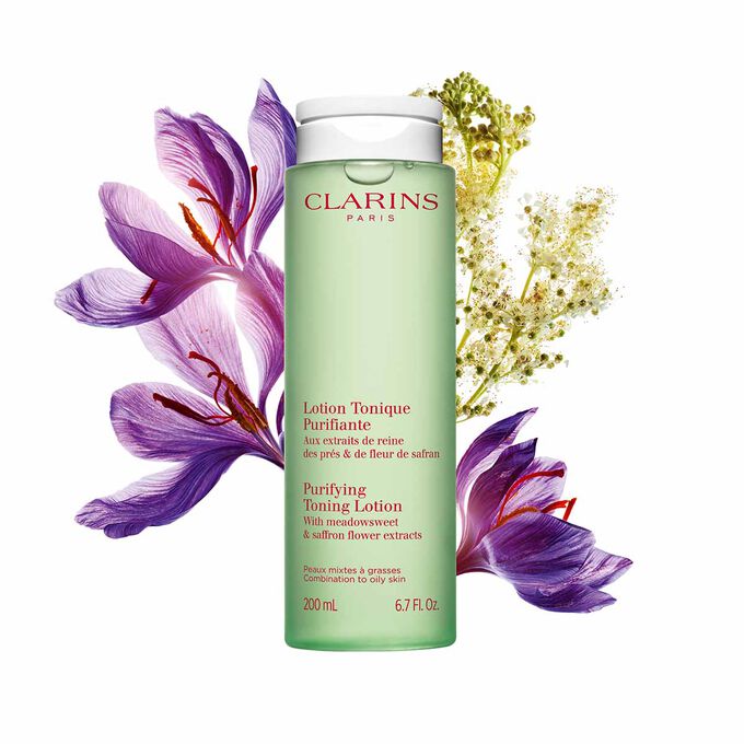 Packshot of the face lotion green bottle next to a saffron flower and meadowsweet on a light green background