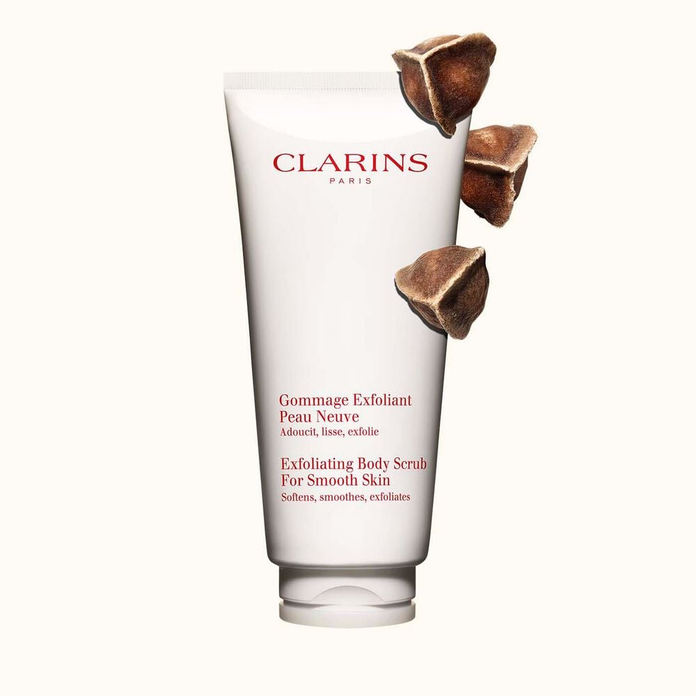 Packshot of Clarins Exfoliating Body Scrub for Smooth Skin placed next to moringa nuts on a light beige background