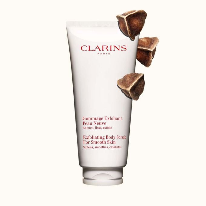 Packshot of Clarins Exfoliating Body Scrub for Smooth Skin placed next to moringa nuts on a light beige background
