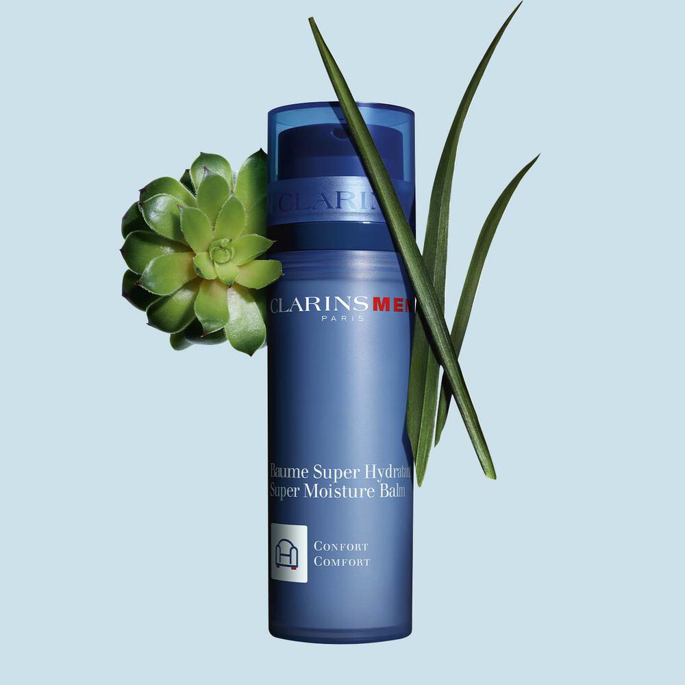 Packshot of a pump bottle of ClarinsMen Super Moisture Balm close to gymnena and bison grass on a blue background.