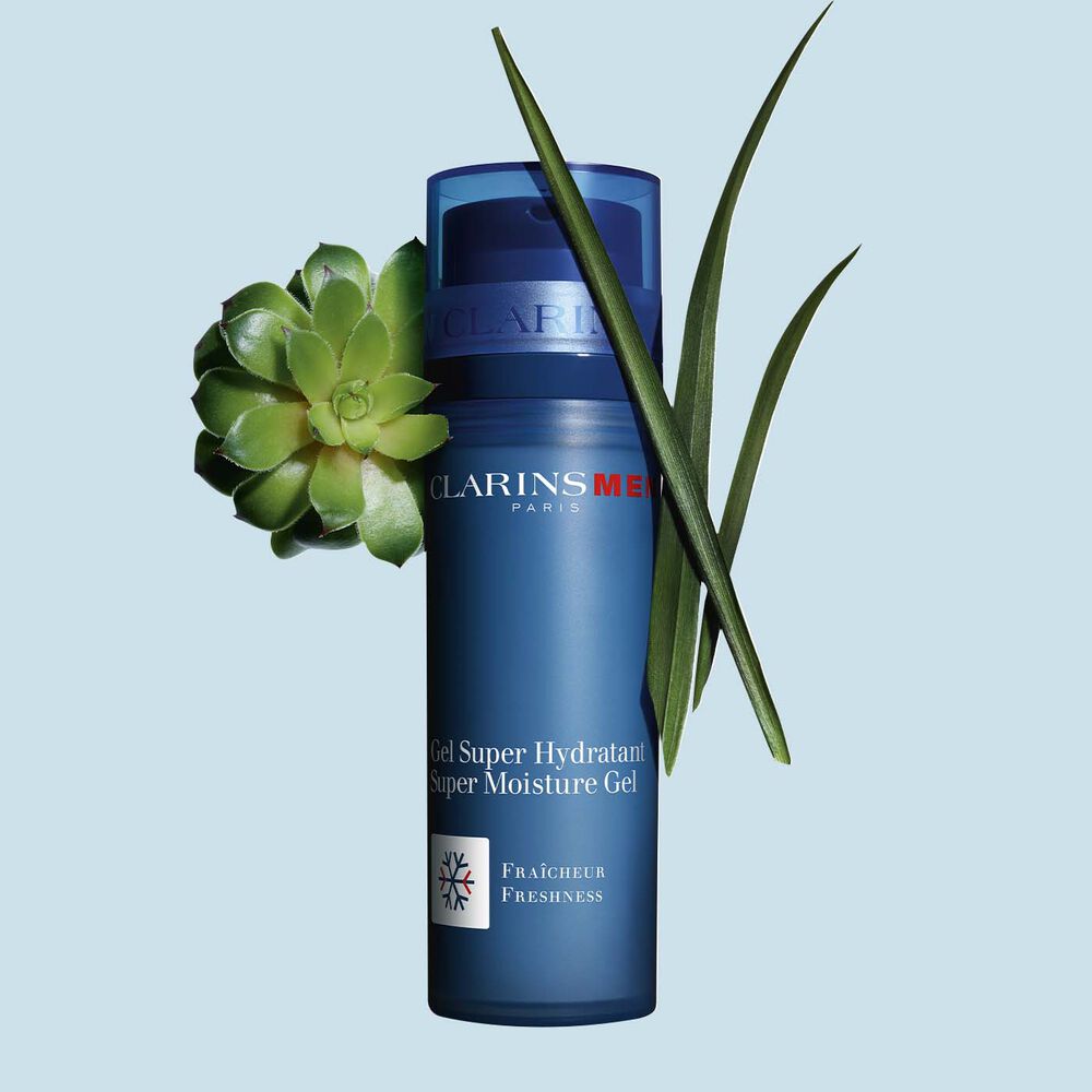 Packshot of a pump bottle of the Men Super Moisture Gel by Clarins close to gymnena and bison grass on a blue background.