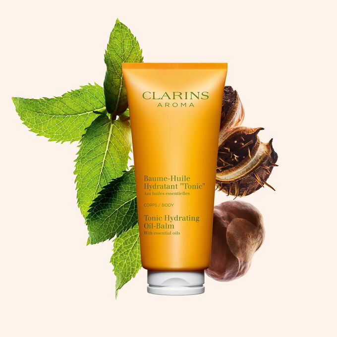Packshot of a tube of Clarins Tonic Hydrating Oil-balm, close to some mint leaves and shea seeds on a peach background.