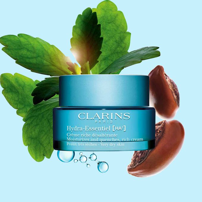 Packshot of Clarins Hydra-Essentiel Rich Cream close to some shea nuts and a kalanchoe leave on a blue background.