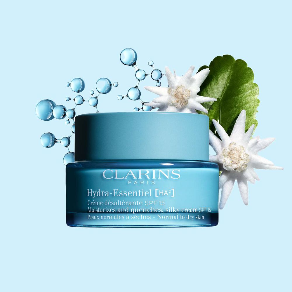 Packshot of Clarins Hydra-Essentiel SPF15 close to some edelweiss flowers on a blue background.