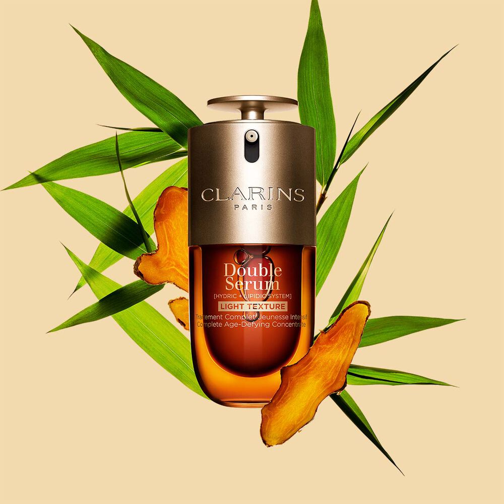 A 30ml bottle of Clarins Double Serum Light Texture among turmeric and proven&ccedil;al reed leaves against an orange background.