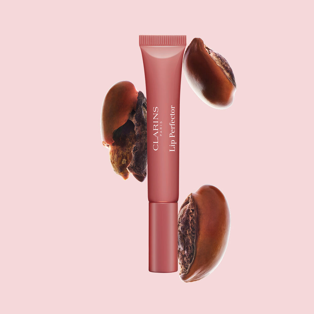Plumping lip perfector tube shown with raw shea seeds to highlight the intense lip care formula for deep nourishment effect