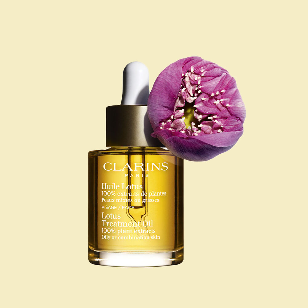 Packshot of a bottle of Clarins Lotus Face Treatment Oil close to a lotus flower on a pale yellow background.