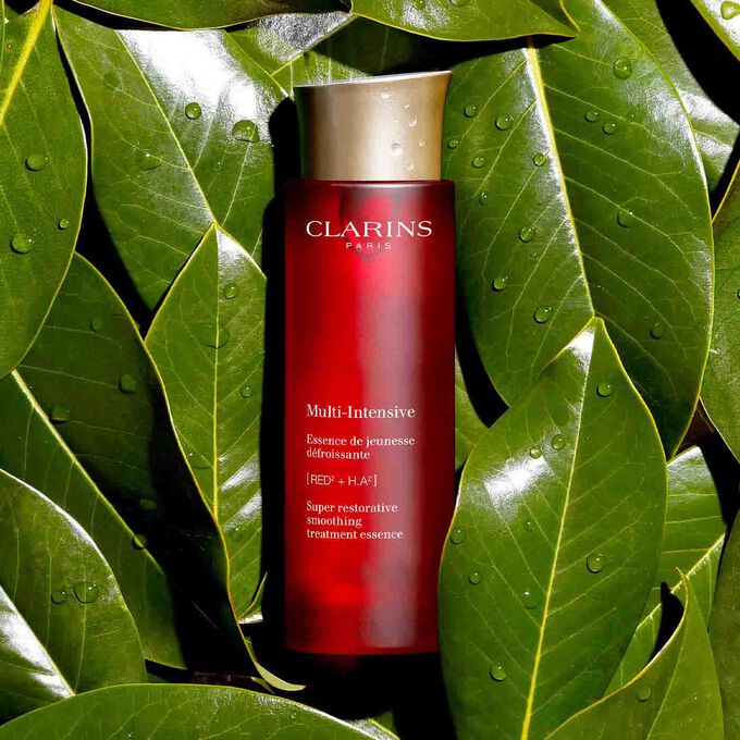 Packshot of Clarins Super Restorative Treatment Essence among Harungana leaves, highlighting 98% natural origin ingredients.