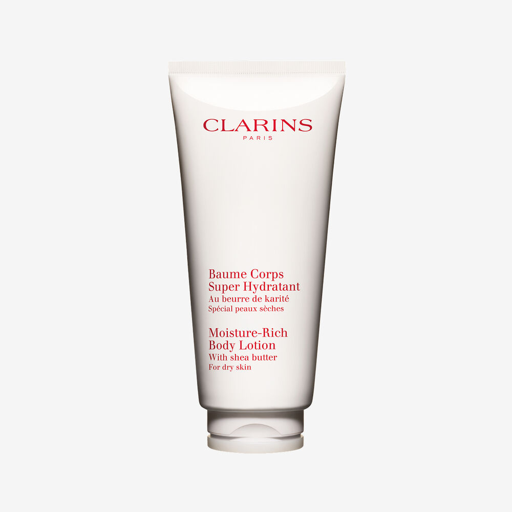 Clarins moisture rich body lotion tube displayed with natural shea butter shells on an elegant white backdrop.